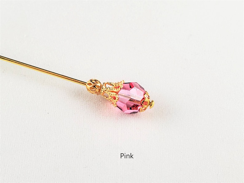 May include: A gold pin with a pink faceted glass bead and a gold filigree design. The pin is on a white background. Pink.