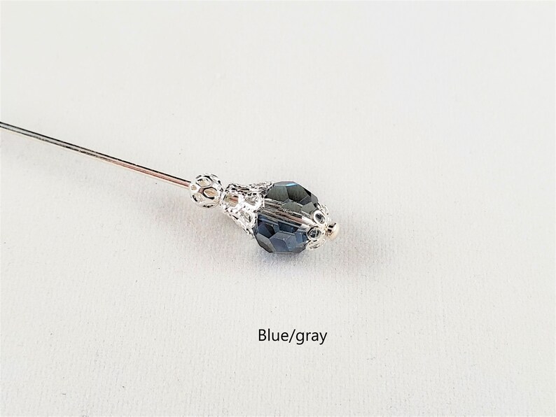 May include: A silver pin with a blue/gray faceted glass bead. The bead is set in a silver filigree design.