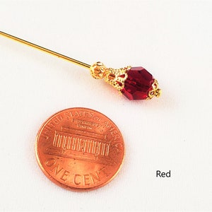 May include: A gold pin with a red glass bead. The pin is about the size of a US penny.