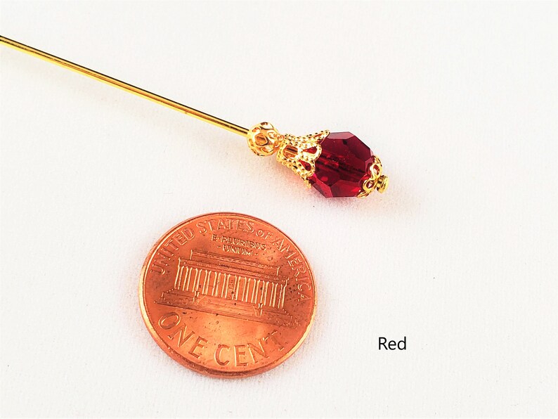 May include: A gold pin with a red glass bead. The pin is about the size of a US penny.