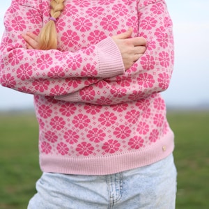 Puede incluir: Un suéter rosa y blanco con estampado y cuello alto. El suéter tiene un diseño floral.