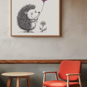 May include: A framed illustration of a smiling hedgehog holding a colorful balloon. A butterfly hovers nearby. A daisy grows at the hedgehog's feet. The artwork is in a wooden frame, hanging on a neutral-colored wall. A round table and a red chair are in the foreground.