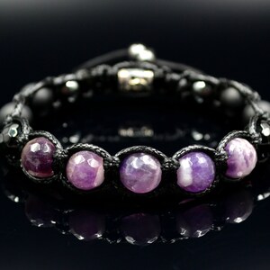 May include: A handcrafted bracelet featuring faceted purple gemstones and black beads, strung on a black cord. The bracelet has a sliding knot closure for adjustable sizing. The gemstones are a vibrant purple color.