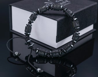 May include: Black lava stone bracelet with a black cord and silver beads. The bracelet is in a black box with a white interior.