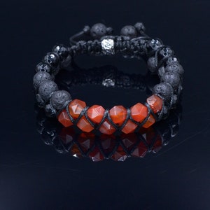 May include: A black lava rock and carnelian gemstone bracelet with a silver bead accent. The bracelet is made with black cord and has a macrame knot closure.