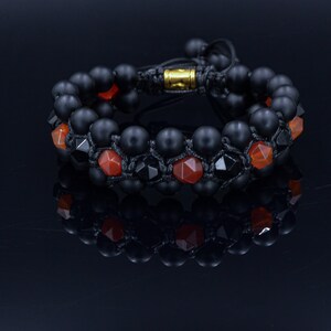May include: A black onyx and carnelian beaded bracelet with a black cord and gold clasp. The bracelet is made of two rows of beads, with the carnelian beads interspersed with the onyx beads.