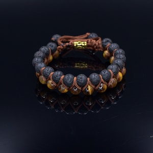 Peut inclure: Un bracelet en perles brunes et noires avec un fermoir doré. Le bracelet est composé de perles de lave et d'œil de tigre.