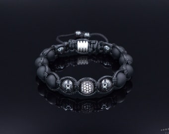 May include: A black beaded bracelet with a macrame design. The bracelet features matte black beads, silver-toned accents, and a central bead encrusted with small, clear crystals. The bracelet is adjustable.