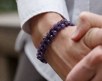 May include: A close-up of a person's wrist wearing a purple amethyst beaded bracelet. The bracelet is made of small, round beads that are strung together on a thin cord.