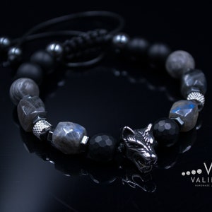 May include: A black beaded bracelet with a silver wolf charm. The beads are made of black onyx, labradorite, and hematite. The bracelet is tied with a black cord.