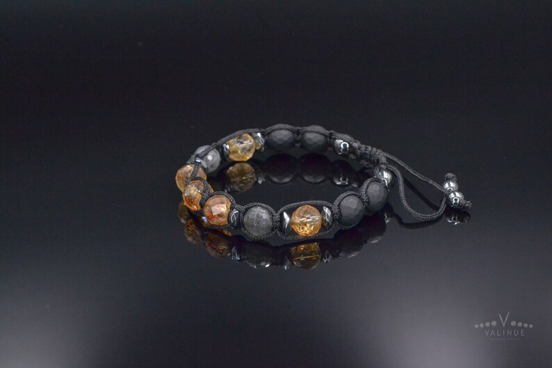 Peut inclure: Un bracelet en perles noires avec des perles de pierres pr&eacute;cieuses brunes et grises. Le bracelet est dot&eacute; d'un cordon noir avec un n&oelig;ud coulissant pour ajuster la taille.