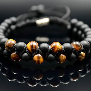 May include: A black and brown beaded bracelet with a braided cord closure. The bracelet features alternating black and tiger's eye beads.