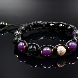 May include: A black cord bracelet with purple and black beads, and a single rose gold bead with clear rhinestones.