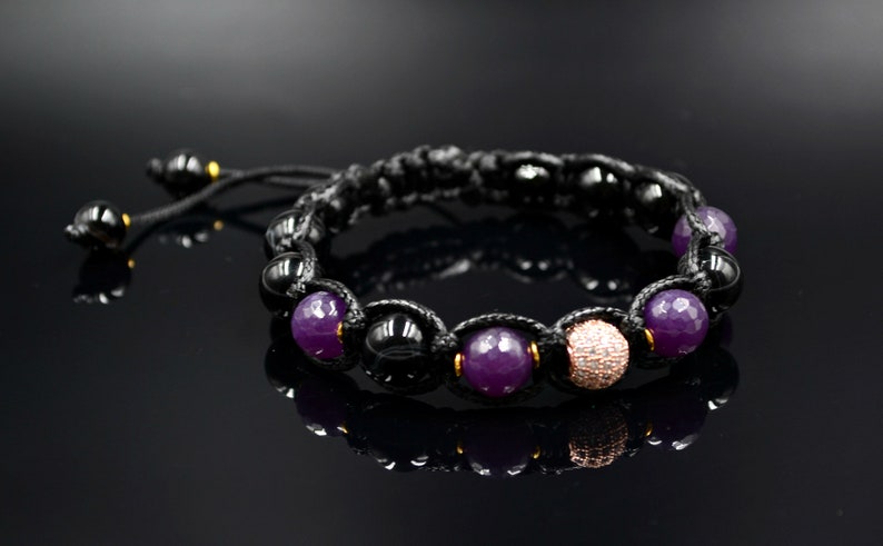 May include: A black cord bracelet with purple and black beads, and a single rose gold bead with clear rhinestones.