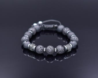 Könnte beinhalten: Ein graues Perlenarmband mit silbernen Akzenten. Das Armband besteht aus Lava- und Hämatitperlen.