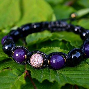 May include: A black cord bracelet with purple and black beads, and a single round bead with clear rhinestones.