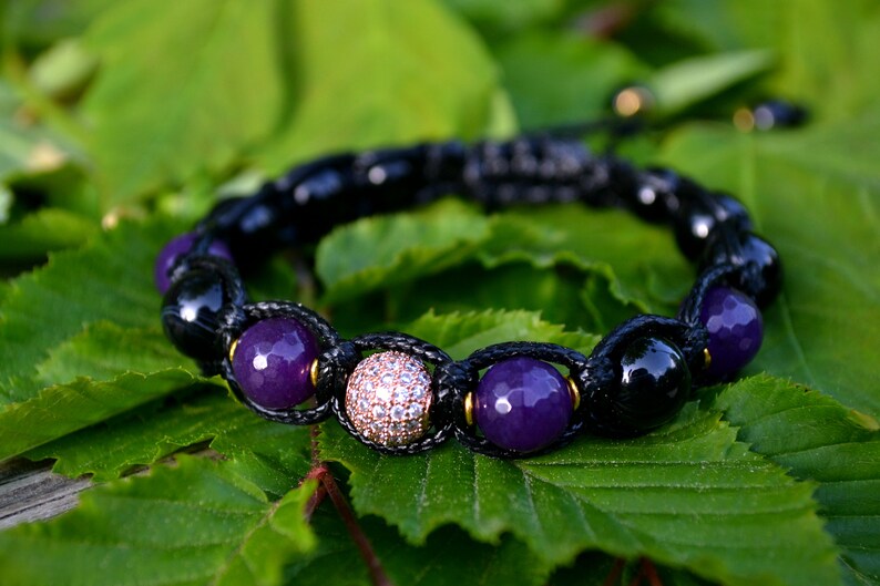 May include: A black cord bracelet with purple and black beads, and a single round bead with clear rhinestones.