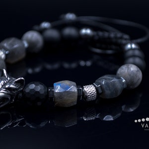 May include: A black and grey beaded bracelet with a silver wolf head charm. The bracelet is made with black onyx, labradorite, and silver beads.