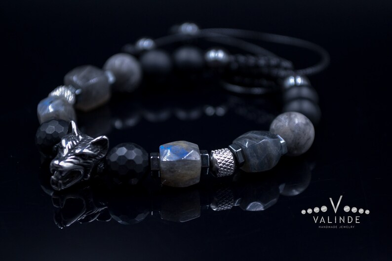 May include: A black and grey beaded bracelet with a silver wolf head charm. The bracelet is made with black onyx, labradorite, and silver beads.