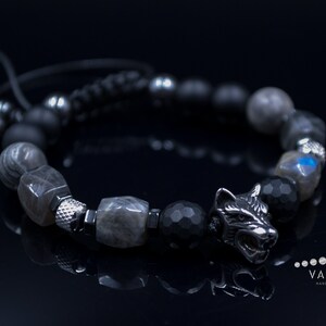 May include: A black and silver bracelet with a wolf head charm. The bracelet is made with black and grey beads and a black cord.