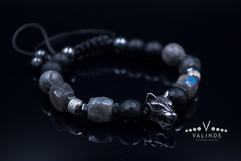 May include: A black and silver bracelet with a wolf head charm. The bracelet is made with black and grey beads and a black cord.