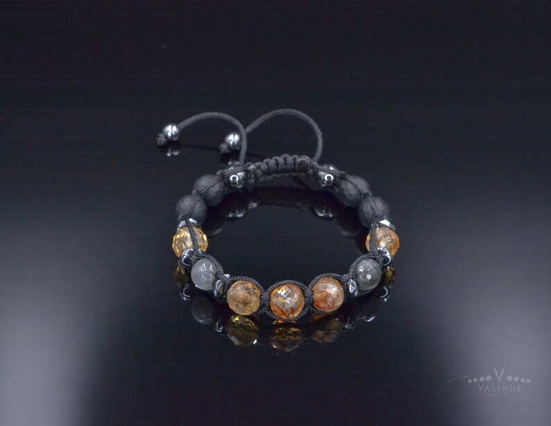 Peut inclure: Un bracelet en cordon noir avec des perles grises et ambr&eacute;es. Le bracelet est nou&eacute; et poss&egrave;de une perle coulissante pour ajuster la taille.