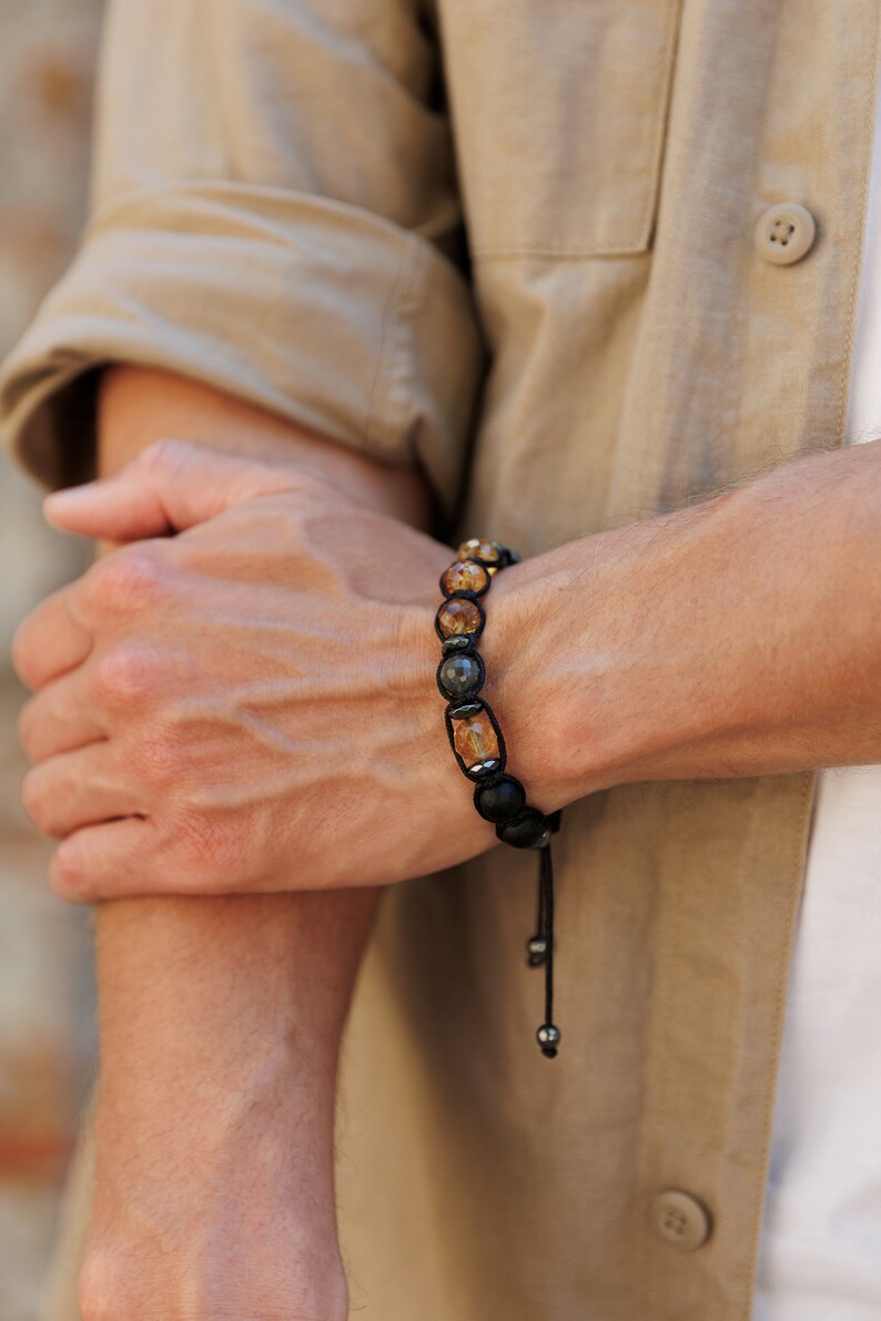 Peut inclure: Un bracelet en perles noires avec des perles de pierres pr&eacute;cieuses brunes et grises. Le bracelet a un cordon noir avec des perles argent&eacute;es.
