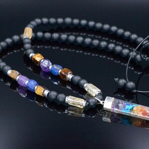 May include: A black beaded necklace with colorful gemstone accents. The necklace features a variety of stones in shades of purple, blue, yellow, and orange, and a clear rectangular pendant with a rainbow design. The necklace is displayed on a reflective black surface.