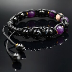 May include: Black and purple beaded bracelet with a black cord and gold accents. The bracelet has a sliding knot closure.