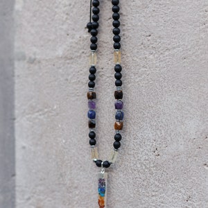 May include: A black beaded necklace with a variety of gemstones and a clear pendant. The necklace features black beads, interspersed with colorful gemstones and a clear rectangular pendant filled with colorful stones.