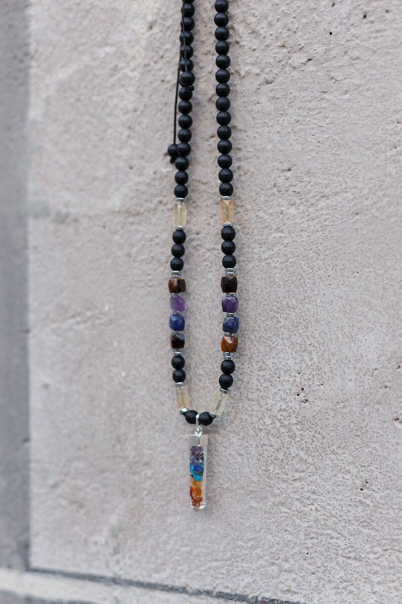 May include: A black beaded necklace with a variety of gemstones and a clear pendant. The necklace features black beads, interspersed with colorful gemstones and a clear rectangular pendant filled with colorful stones.
