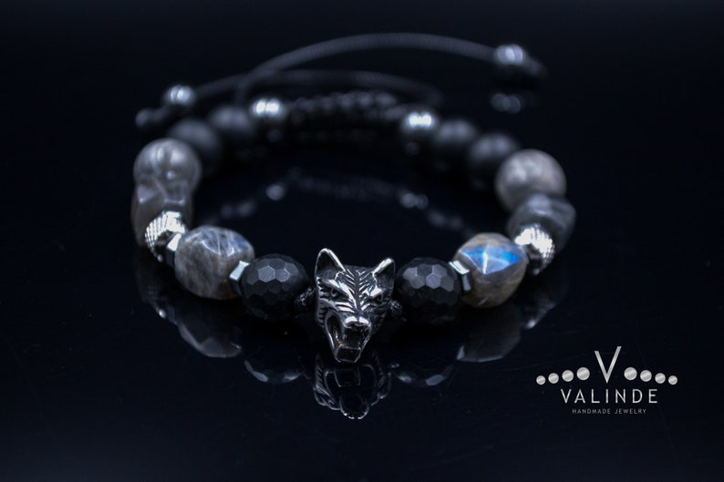 May include: A black and silver beaded bracelet with a wolf head charm. The beads are made of black onyx and labradorite. The bracelet is adjustable and has a black cord.