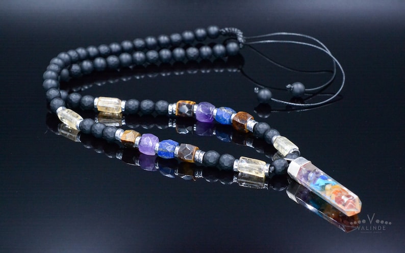 May include: A black beaded necklace with a variety of colorful gemstones and a crystal pendant. The necklace features a mix of black matte beads, clear and colorful gemstones, and a long, multi-colored crystal pendant.