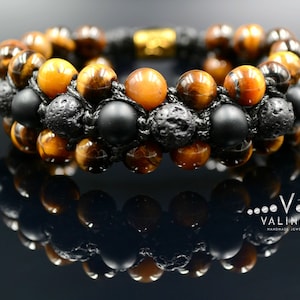 May include: A double-layered bracelet with tiger's eye, black lava rock, and black onyx beads. The bracelet is made with black cord and has a gold clasp.