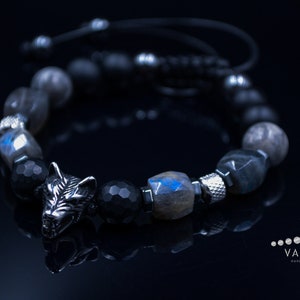 May include: A black beaded bracelet with a silver wolf charm. The beads are made of black onyx, labradorite and haematite. The bracelet is tied with a black cord.