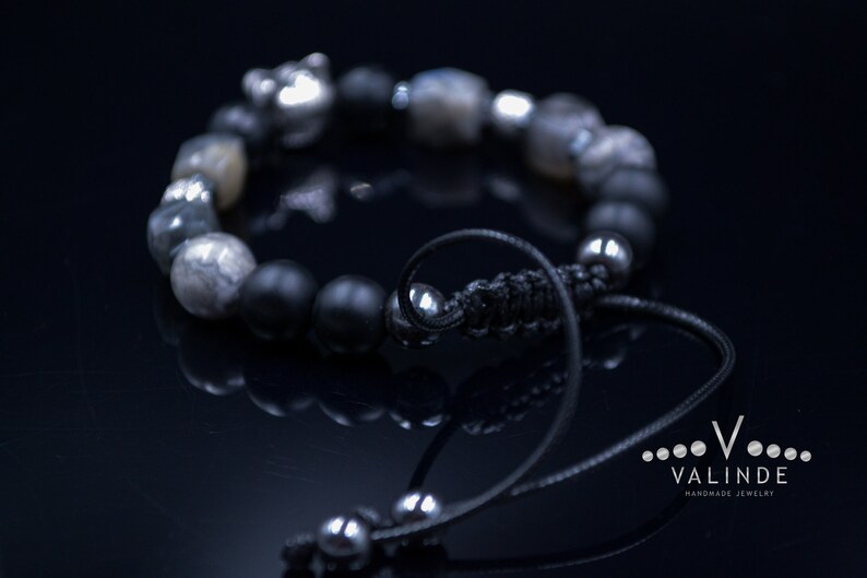 May include: A black and silver beaded bracelet with a silver charm. The bracelet has a black cord with a silver bead at the end.