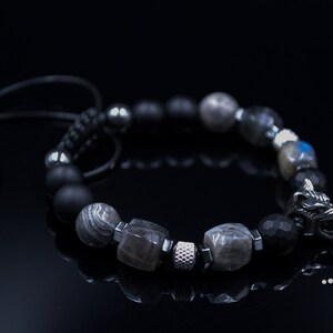May include: A black beaded bracelet with a silver wolf head charm. The bracelet features black, grey, and silver beads.