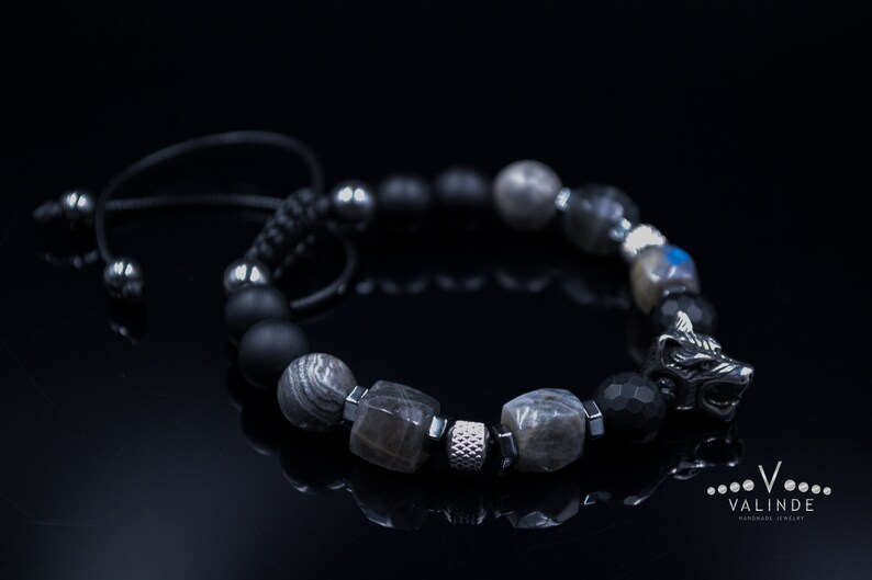 May include: A black beaded bracelet with a silver wolf head charm. The bracelet features black, grey, and silver beads.
