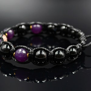 May include: A black and purple beaded bracelet with a black cord and gold accents. The bracelet has a sliding knot closure.
