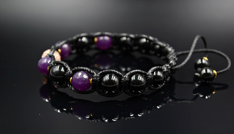 May include: A black and purple beaded bracelet with a black cord and gold accents. The bracelet has a sliding knot closure.