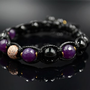 May include: A black cord bracelet with purple and black beads, and a rose gold bead with clear rhinestones.
