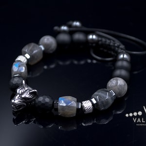May include: A black and silver beaded bracelet with a wolf head charm. The bracelet features black onyx, labradorite and hematite beads. The wolf head charm is made of metal and has a detailed design. The bracelet is tied with a black cord.