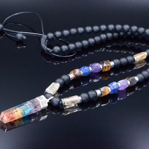 May include: A black beaded necklace with a rainbow-colored crystal pendant. The necklace features various gemstone beads in colors like purple, blue, and yellow. The pendant is a clear crystal with layers of rainbow colors. The necklace is on a reflective black surface.