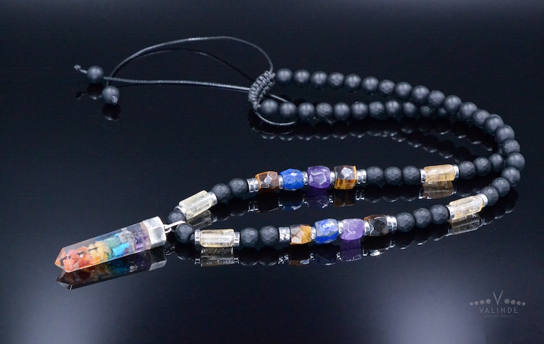 May include: A black beaded necklace with a pendant featuring a rainbow-colored crystal. The necklace includes various colorful gemstones and is designed with a black cord and adjustable knot.