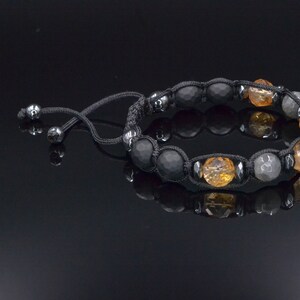 Peut inclure: Un bracelet en cordon noir avec des perles noires, grises et orange. Le bracelet a une fermeture &agrave; n&oelig;ud coulissant.