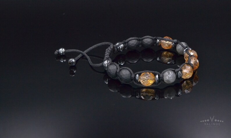 Peut inclure: Un bracelet en cordon noir avec des perles noires, grises et orange. Le bracelet a une fermeture &agrave; n&oelig;ud coulissant.