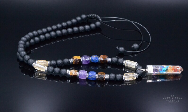 May include: Black beaded necklace with colorful gemstone accents and a clear crystal pendant with rainbow-colored layers. The necklace has a black cord and a silver-colored metal clasp. The pendant is approximately 1.5 inches long.