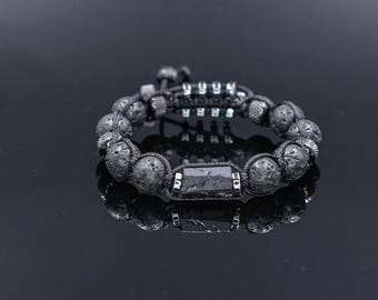 May include: A black lava rock bracelet with a silver metal accent and a black gemstone. The bracelet is on a black reflective surface.