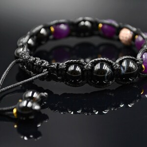 May include: Black and purple beaded bracelet with a black cord and gold accents. The bracelet has a sliding knot closure.