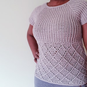May include: A light purple crochet top with a diamond pattern on the bottom. The top has short sleeves and a round neckline.
